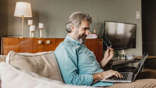 Ein Mann erledigt Zuhause im Wohnzimmer seine Rechnungen mit dem Laptop.